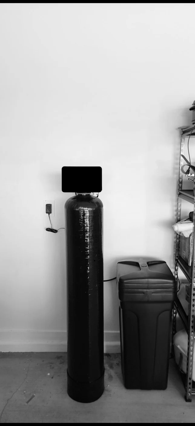 Black whole-home treatment tank and brine tank installed in a garage