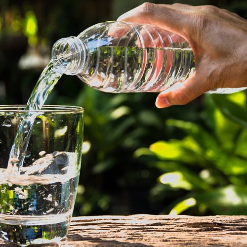 Female hand pouring water from bottle to glass on nature background